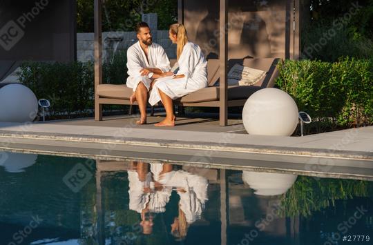 Couple in bathrobes sitting on bench lounger by a pool, reflection in water, outdoor setting in a wellness spa resort   : Stock Photo or Stock Video Download rcfotostock photos, images and assets rcfotostock | RC Photo Stock.: