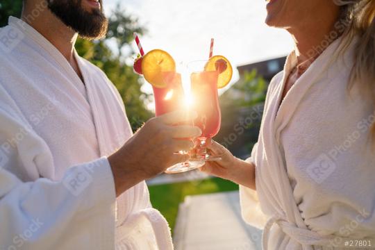 Couple in white bathrobes clinking red cocktails with a sunset behind at spa hotel  : Stock Photo or Stock Video Download rcfotostock photos, images and assets rcfotostock | RC Photo Stock.: