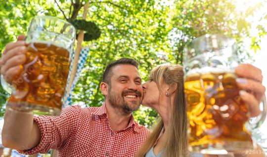 Couple kissing and smiling at camera say cheers or clinking glasses with mug of beer in Bavarian beer garden or oktoberfest  : Stock Photo or Stock Video Download rcfotostock photos, images and assets rcfotostock | RC Photo Stock.: