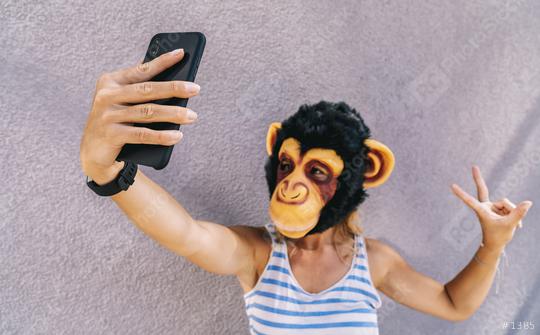 Crazy young woman with monkey mask stands on a gray wall and use a smartphone to take a selfie pic.  : Stock Photo or Stock Video Download rcfotostock photos, images and assets rcfotostock | RC Photo Stock.:
