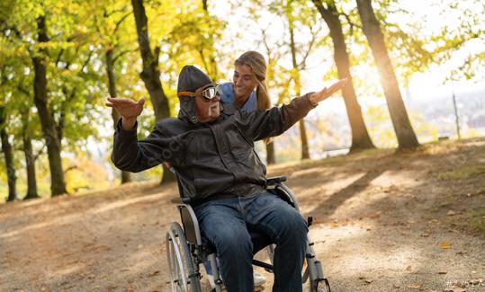 Elderly man in aviator gear and a nurse enjoying a playful moment in a park, with sunlight filtering through autumn trees  : Stock Photo or Stock Video Download rcfotostock photos, images and assets rcfotostock | RC Photo Stock.: