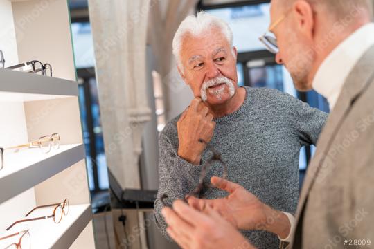 Elderly man pondering over eyeglasses with optician in optical store  : Stock Photo or Stock Video Download rcfotostock photos, images and assets rcfotostock | RC Photo Stock.: