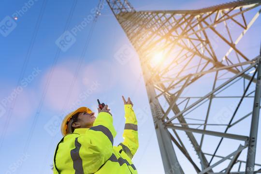 Electrical female engineer talking in a walkie talkie and pointing to control a high voltage electricity pylon. Close-up Electrical power lines and towers with bright sun  : Stock Photo or Stock Video Download rcfotostock photos, images and assets rcfotostock | RC Photo Stock.: