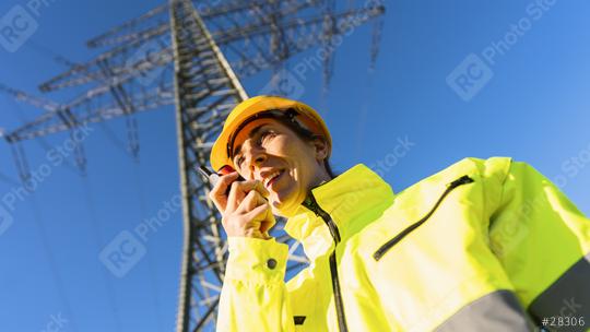 Electrical female engineer talking in a walkie talkie to control a high voltage electricity pylon. Electrical power lines and towers with bright sun  : Stock Photo or Stock Video Download rcfotostock photos, images and assets rcfotostock | RC Photo Stock.: