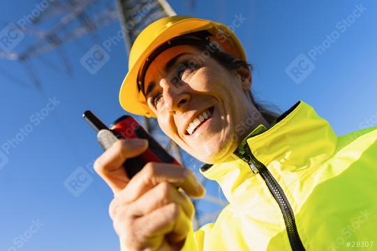 Electrical female engineer talking in a walkie talkie to control a high voltage electricity pylon. Close-up Electrical power lines and towers with bright sun  : Stock Photo or Stock Video Download rcfotostock photos, images and assets rcfotostock | RC Photo Stock.: