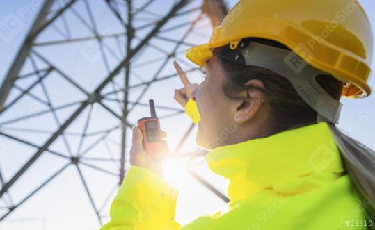 Electrical female engineer using walkie talkie to control a high voltage electricity pylon. Electrical power lines and towers with bright sun  : Stock Photo or Stock Video Download rcfotostock photos, images and assets rcfotostock | RC Photo Stock.: