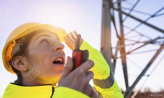 Electrical female engineer watching up and talking in a walkie talkie to control a high voltage electricity pylon. Electrical power lines and towers with bright sun  : Stock Photo or Stock Video Download rcfotostock photos, images and assets rcfotostock | RC Photo Stock.: