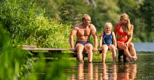 Family sitting on a wooden dock by a lake, dangling their feet in the water, surrounded by lush greenery in bavaria germany  : Stock Photo or Stock Video Download rcfotostock photos, images and assets rcfotostock | RC Photo Stock.: