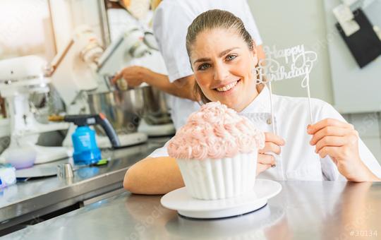 female confectioner smiling proudly and decorating big Birthday cake muffin with candies at pastry bakery  : Stock Photo or Stock Video Download rcfotostock photos, images and assets rcfotostock | RC Photo Stock.: