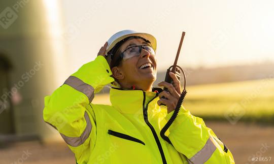 female engineer with safety jacket standing in front of a wind turbine talking in a walkie talkie to checking wind turbine system  : Stock Photo or Stock Video Download rcfotostock photos, images and assets rcfotostock | RC Photo Stock.: