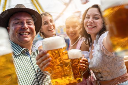 Four friends happily toasting with beer mugs at an outdoor fairground with amusement rides in the background at a vibrant Oktoberfest or dult in germany  : Stock Photo or Stock Video Download rcfotostock photos, images and assets rcfotostock | RC Photo Stock.: