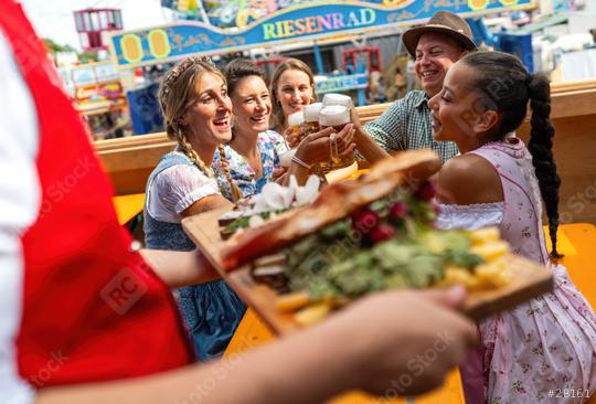 Friends at oktoberfest festival table receiving a tray of traditional food, joyfully toasting with beer, amusement rides in the background in munich germany  : Stock Photo or Stock Video Download rcfotostock photos, images and assets rcfotostock | RC Photo Stock.: