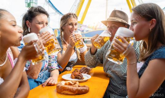 Friends enjoying bavarian beer at oktoberfest festival on a beer tent table with a pretzel and grilled chicken, amusement rides visible  : Stock Photo or Stock Video Download rcfotostock photos, images and assets rcfotostock | RC Photo Stock.: