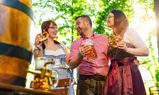 Friends girls and man, having fun in beer garden holding beer mug and traditional Bavaria pretzels in front of a wooden beer barrel at Oktoberfest, Munich, Germany  : Stock Photo or Stock Video Download rcfotostock photos, images and assets rcfotostock | RC Photo Stock.: