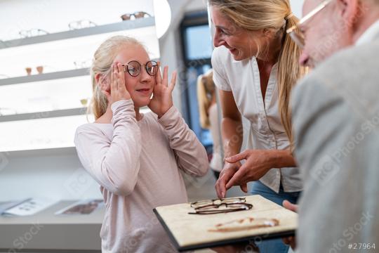 Girl trying glasses with assistance. Her mother is smiling. The optician advising in his eyewear shop. It is family eyecare moment
.  : Stock Photo or Stock Video Download rcfotostock photos, images and assets rcfotostock | RC Photo Stock.: