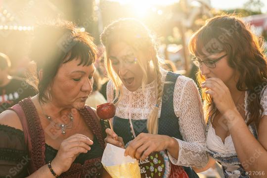 Girlfriends eat roasted almonds together from the paper bag in front of the gingerbread stand at a Bavarian fair or oktoberfest or duld in national costume or Dirndl  : Stock Photo or Stock Video Download rcfotostock photos, images and assets rcfotostock | RC Photo Stock.: