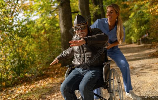 grandpa in aviator attire and goggles mimics flying, pushed by a laughing nurse in an autumn park. nursery home concept image   : Stock Photo or Stock Video Download rcfotostock photos, images and assets rcfotostock | RC Photo Stock.: