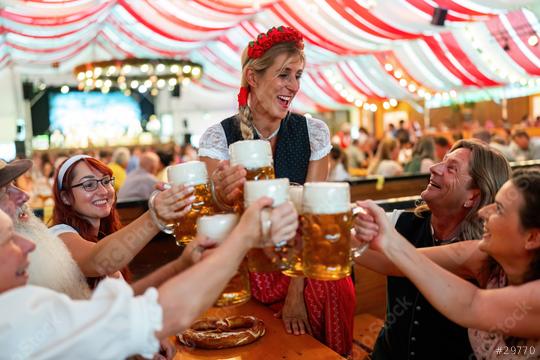 group of frienfs in traditional Bavarian attire toasting with beer steins and enjoying a festive indoor event in an Oktoberfest tent with red and white drapes in the background  : Stock Photo or Stock Video Download rcfotostock photos, images and assets rcfotostock | RC Photo Stock.: