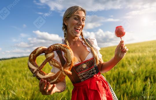 Happy Bavarian woman in tracht holding a pretzel and a candy apple, laughing in a sunny wheat field celebrating Oktoberfest ferstival in munich  : Stock Photo or Stock Video Download rcfotostock photos, images and assets rcfotostock | RC Photo Stock.: