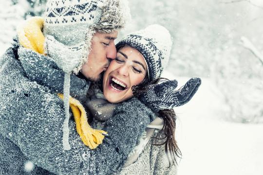 Happy couple embracing in a snowy winter setting, wearing cozy sweaters, scarves, and hats, with the man kissing the woman on the cheek as they laugh in a joyful, snowy moment  : Stock Photo or Stock Video Download rcfotostock photos, images and assets rcfotostock | RC Photo Stock.: