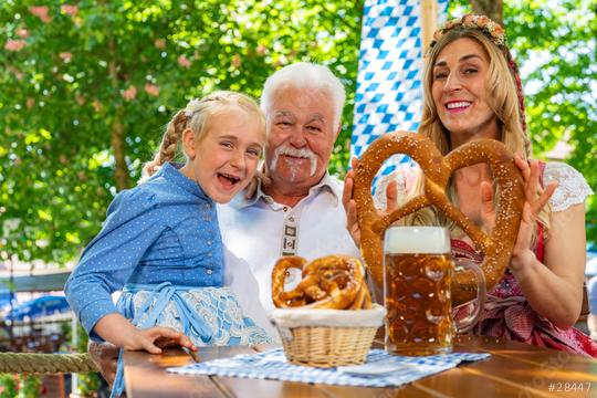 Happy family in proper Tracht holding big pretzel and drinking in Bavarian beer garden at Oktoberfest, folk or beer festival in germany   : Stock Photo or Stock Video Download rcfotostock photos, images and assets rcfotostock | RC Photo Stock.: