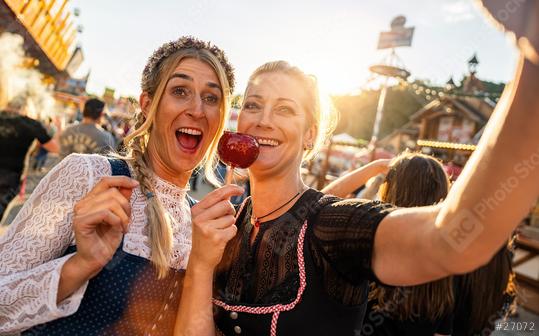 Happy girlfriends eating candy apple on a Bavarian fair or oktoberfest or duld in national costume or Dirndl in germany   : Stock Photo or Stock Video Download rcfotostock photos, images and assets rcfotostock | RC Photo Stock.: