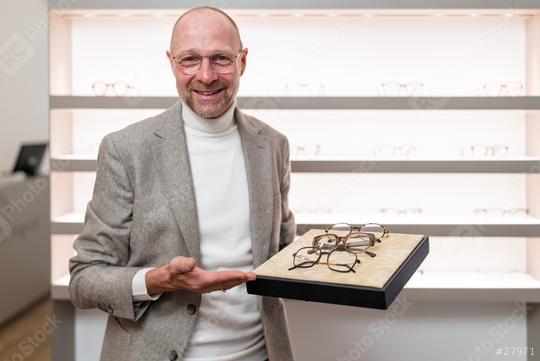 Happy optician presenting a tray with various eyeglasses at an optical store. Shelves of glasses are behind.  : Stock Photo or Stock Video Download rcfotostock photos, images and assets rcfotostock | RC Photo Stock.: