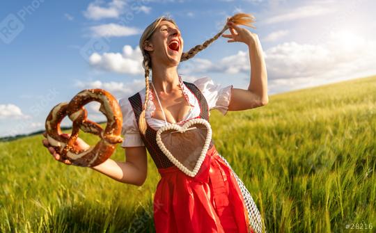 Happy woman in Bavarian dirndl with a gingerbread heart, laughing and holding a pretzel in a wheat field celebrating Oktoberfest or dult festival in munich.  : Stock Photo or Stock Video Download rcfotostock photos, images and assets rcfotostock | RC Photo Stock.: