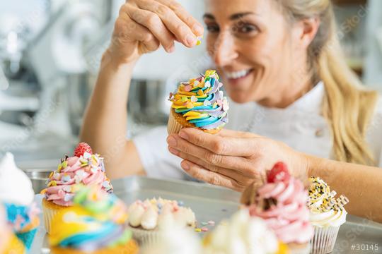 happy women in pastry bakery as confectioner sprinkles candies topping on a colorful muffin by hand  : Stock Photo or Stock Video Download rcfotostock photos, images and assets rcfotostock | RC Photo Stock.: