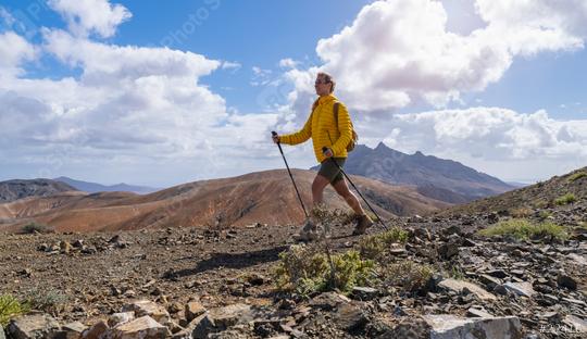 Hiker in yellow jacket walking on mountain trail with cloudy sky and peak in distance  : Stock Photo or Stock Video Download rcfotostock photos, images and assets rcfotostock | RC Photo Stock.: