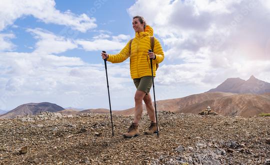 Hiker in yellow jacket with trekking poles on a rocky mountain trail, mountains in the back  : Stock Photo or Stock Video Download rcfotostock photos, images and assets rcfotostock | RC Photo Stock.: