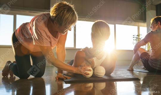 Instructor assisting yoga student with posture with massage ball, sunny studio, reflective floor  : Stock Photo or Stock Video Download rcfotostock photos, images and assets rcfotostock | RC Photo Stock.: