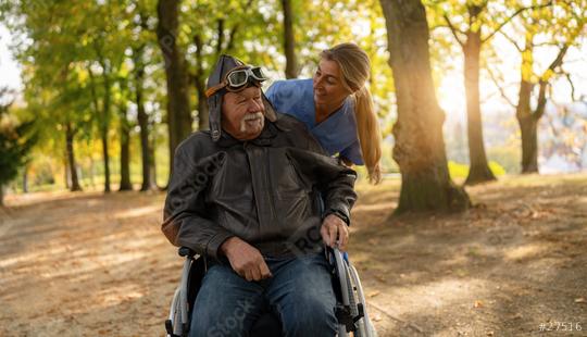 Joyful elderly man in aviator gear looking up while being pushed in a wheelchair by a smiling nurse in a sunlit park. Dementia retirement home concept image  : Stock Photo or Stock Video Download rcfotostock photos, images and assets rcfotostock | RC Photo Stock.: