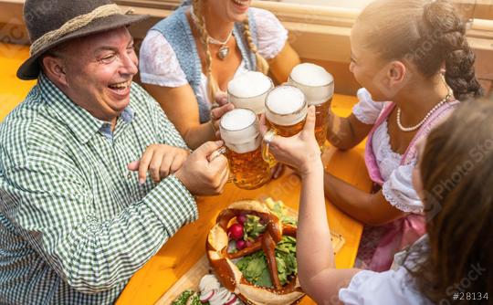 joyful group of friends clinking beer mugs at a table with a large pretzel, in a beer tent and celebrating at a Oktoberfest or dult  : Stock Photo or Stock Video Download rcfotostock photos, images and assets rcfotostock | RC Photo Stock.: