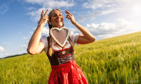 Joyful woman in Bavarian costume placing a gingerbread heart around her head, in a wheat field celebrating Oktoberfest in munich, with copyspace for your individual text.  : Stock Photo or Stock Video Download rcfotostock photos, images and assets rcfotostock | RC Photo Stock.: