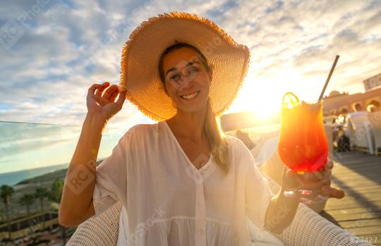 Joyful woman in straw hat offering a cocktail at tropical beach hotel with sunset in the background  : Stock Photo or Stock Video Download rcfotostock photos, images and assets rcfotostock | RC Photo Stock.: