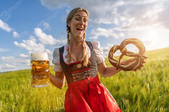 Joyful woman in traditional Bavarian dress holding beer and pretzel in a sunny field ready for Oktoberfest festival in munich, germany  : Stock Photo or Stock Video Download rcfotostock photos, images and assets rcfotostock | RC Photo Stock.: