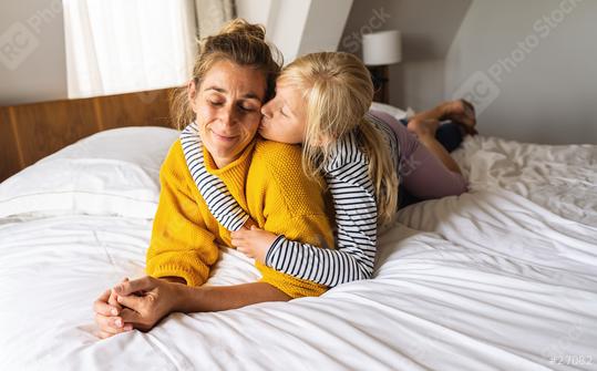 Little girl kissing her mother lying on bed and enjoy the time at home. Mother