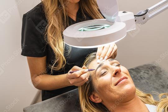 Make-up artist plucks eyebrows with tweezers to a woman. Beautiful thick eyebrows in spa center or cosmetology salon. Makeup and Cosmetology concept image  : Stock Photo or Stock Video Download rcfotostock photos, images and assets rcfotostock | RC Photo Stock.: