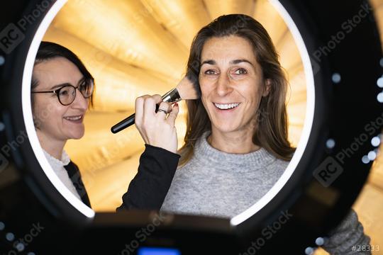 makeup artist powders a models face posing at camera through ring light lamp. Photo shooting with ring light or movie set location  : Stock Photo or Stock Video Download rcfotostock photos, images and assets rcfotostock | RC Photo Stock.: