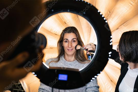 makeup artist powders a models face posing at camera through ring light lamp at a Photo shooting with ring light  : Stock Photo or Stock Video Download rcfotostock photos, images and assets rcfotostock | RC Photo Stock.: