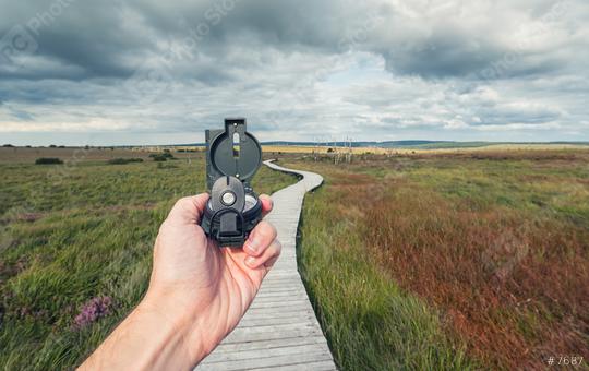 Male traveler holds a compass on background of a bog landscape with wooden trail and cloudy sky, view of hand, pov.  : Stock Photo or Stock Video Download rcfotostock photos, images and assets rcfotostock | RC-Photo-Stock.: