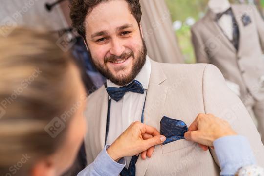 Man being fitted for a suit, tailor adjusts a blue pocket square, both smiling in a wedding store  : Stock Photo or Stock Video Download rcfotostock photos, images and assets rcfotostock | RC Photo Stock.: