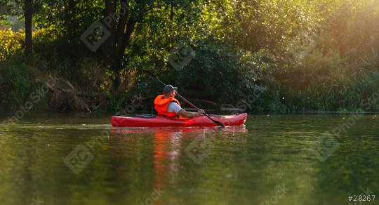 Man in a red kayak paddles serenely on a calm river, surrounded by dense green foliage under a golden sunlight at summer. Kayak Water Sports concept image  : Stock Photo or Stock Video Download rcfotostock photos, images and assets rcfotostock | RC Photo Stock.: