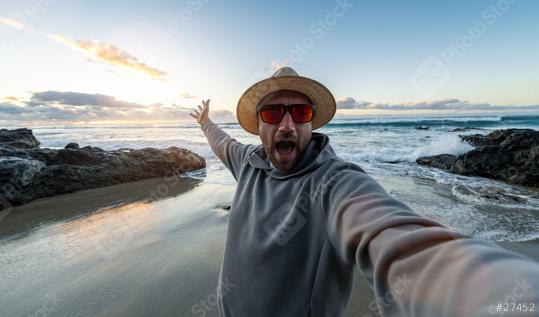 Man in a straw hat and sunglasses taking a selfie on a rocky beach at sunset enjoying summer holidays   : Stock Photo or Stock Video Download rcfotostock photos, images and assets rcfotostock | RC Photo Stock.: