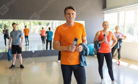 Man in orange shirt holding a water bottle in gym with other people and exercise balls. Teamwork Concept image  : Stock Photo or Stock Video Download rcfotostock photos, images and assets rcfotostock | RC Photo Stock.: