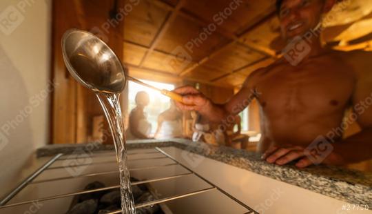 Man pouring water from a sauna ladle onto hot rocks on a sauna stove. People in the background. Finish sauna spa wellness hotel concept image.  : Stock Photo or Stock Video Download rcfotostock photos, images and assets rcfotostock | RC Photo Stock.: