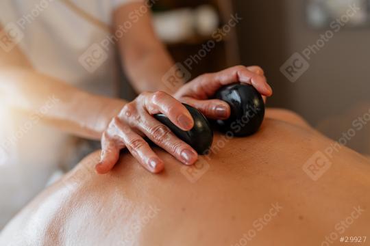 Massage therapist using hot stones on client