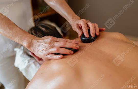 Massage therapist using hot stones on client