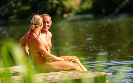 Mature couple intimately sitting together on a wooden dock overlooking the lake, smiling and enjoying the day at summer  : Stock Photo or Stock Video Download rcfotostock photos, images and assets rcfotostock | RC Photo Stock.: